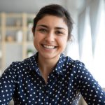 Happy young indian woman blogger applicant teacher sit at home office look at camera doing online job interview during video chat conference call record vlog teaching on webinar in app, webcam view